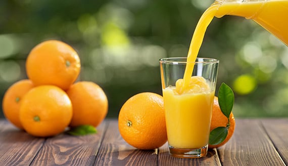 glass of orange juice beng poured with oranges in the background