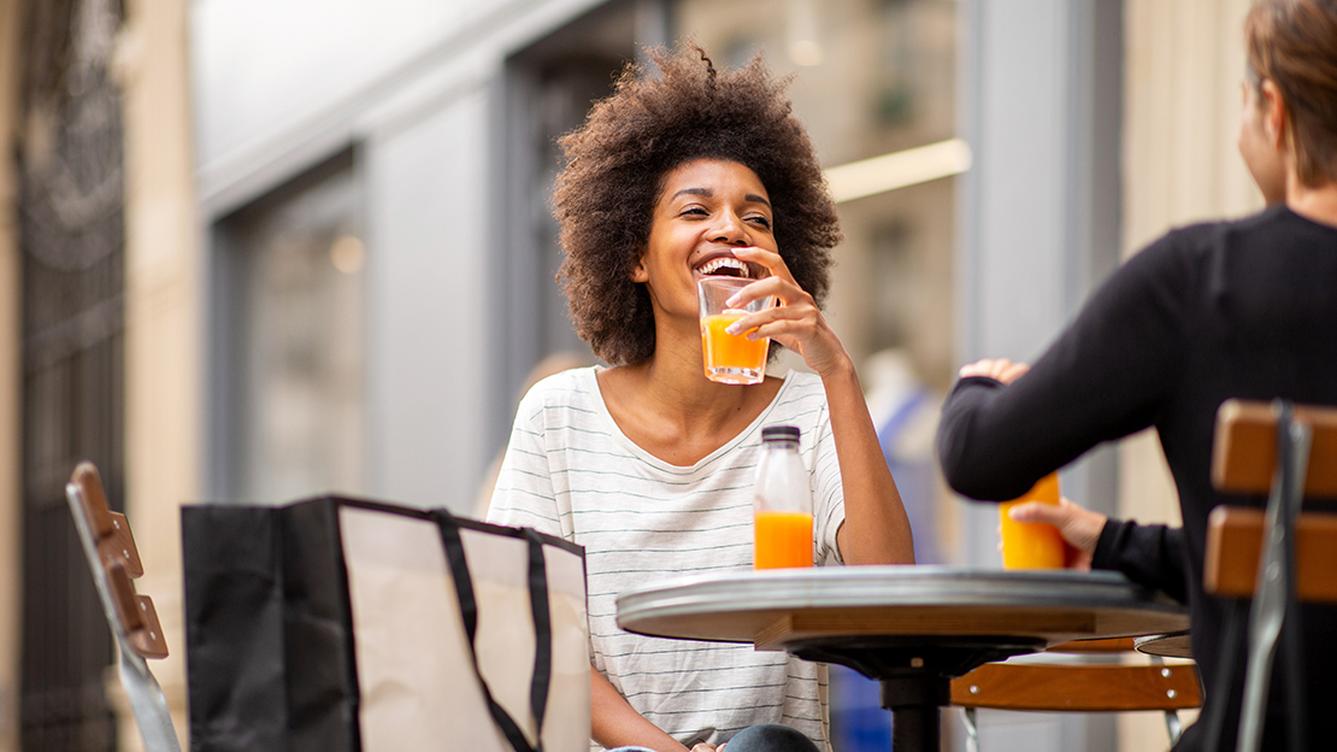 woman drinking an orange drink at a table smiling