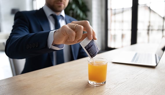 man pouring packet of a powdery mix into orange juice