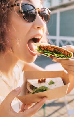 woman in sunglasses eating taco on street