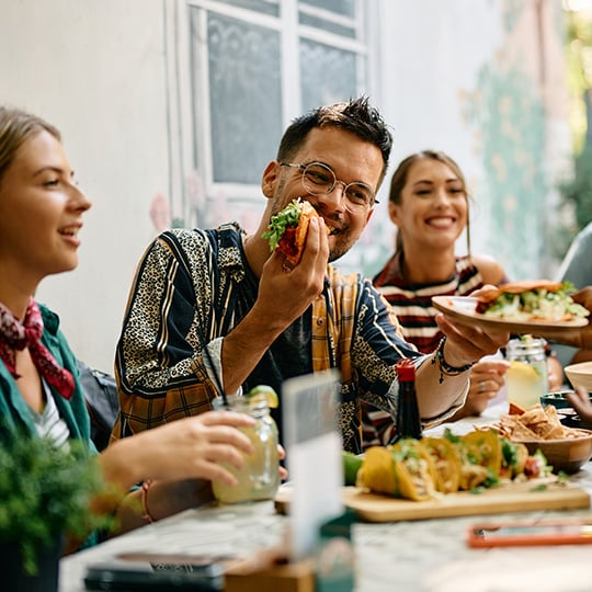 C12 Male and Two Female Friends at Outdoor Table Enjoying a Meal Together