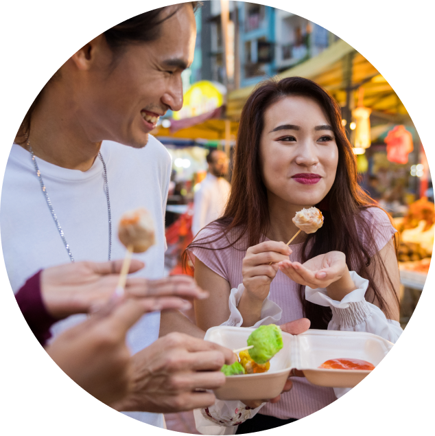 A group of friends huddled together at an outdoor market trying reduced sugar pastries on a stick.