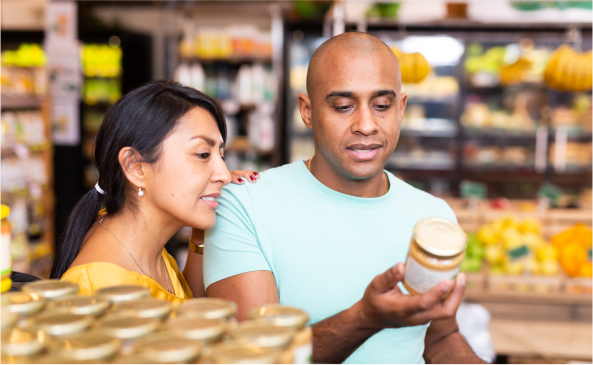 A couple in a grocery store looking over the label of a reduced sugar product in a jar.