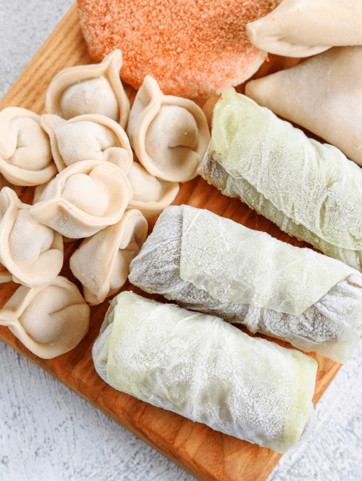 Frozen dumplings and cabbage rolls on a wooden cutting board
